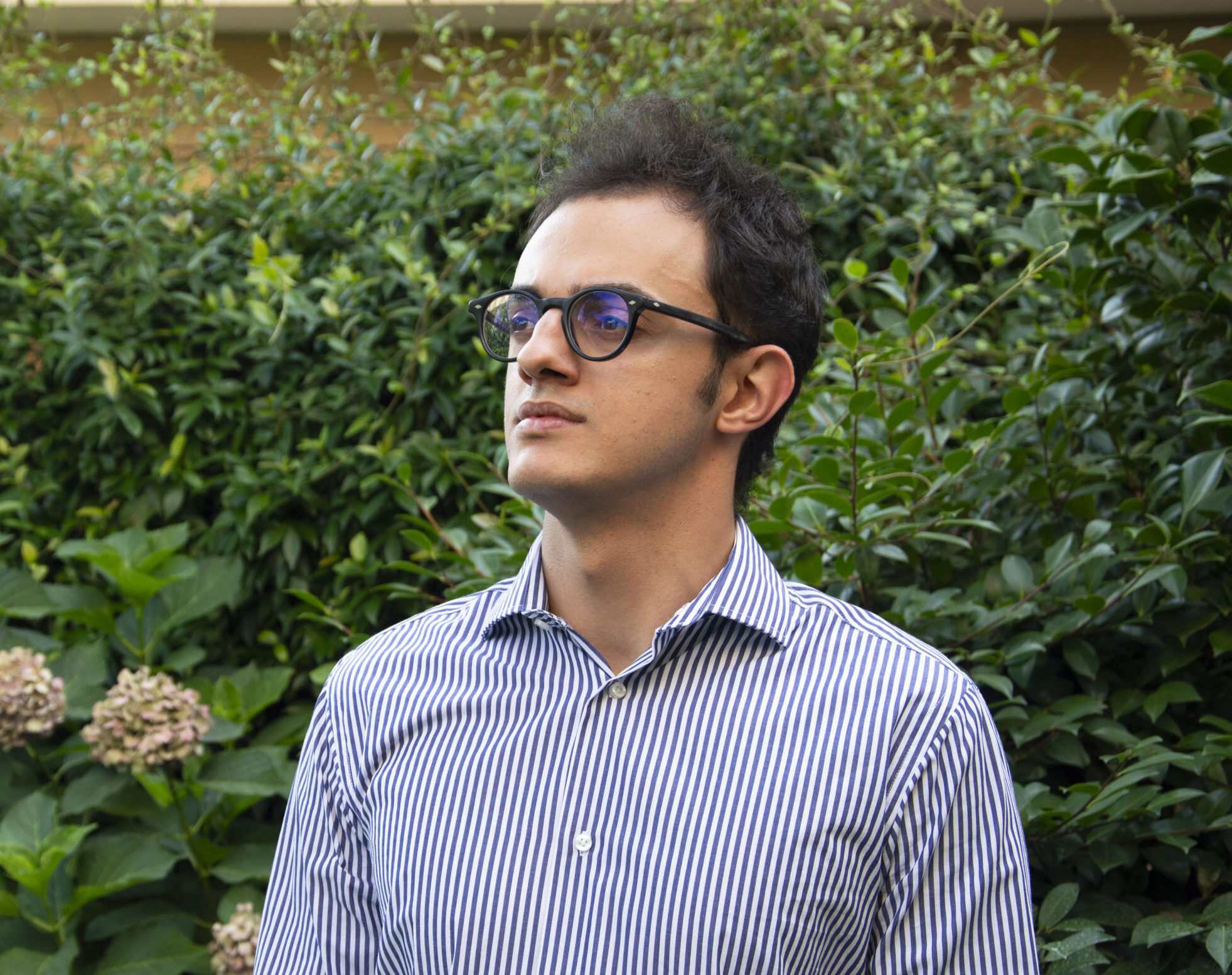 Ritratto professionale di Filippo Bindi, Graphic & Web Designer, con occhiali e camicia a righe all’aperto.